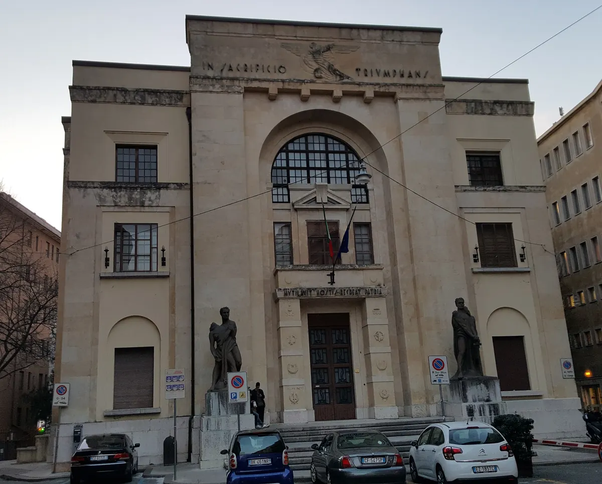 Die steinerne Fassade des Palastes in der Via dei Mutilati mit einem großen Bogenfenster über der Tür und je einer Statue zu beiden Seiten
